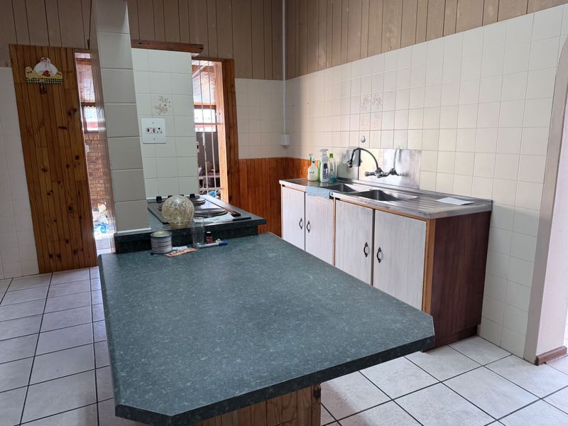A functional kitchen featuring built-in cabinetry, a stainless steel sink, and a central island with a built-in hob, finished with ceramic tiling.