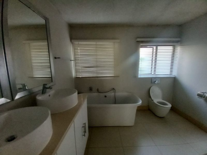 A spacious bathroom featuring a double vanity, a modern freestanding bathtub, and a wall-mounted toilet, with natural light provided by dual windows.