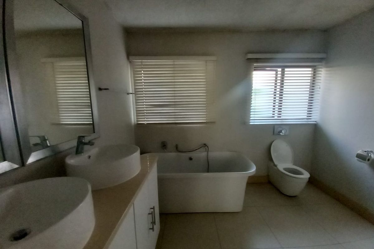 A spacious bathroom featuring a double vanity, a modern freestanding bathtub, and a wall-mounted toilet, with natural light provided by dual windows.