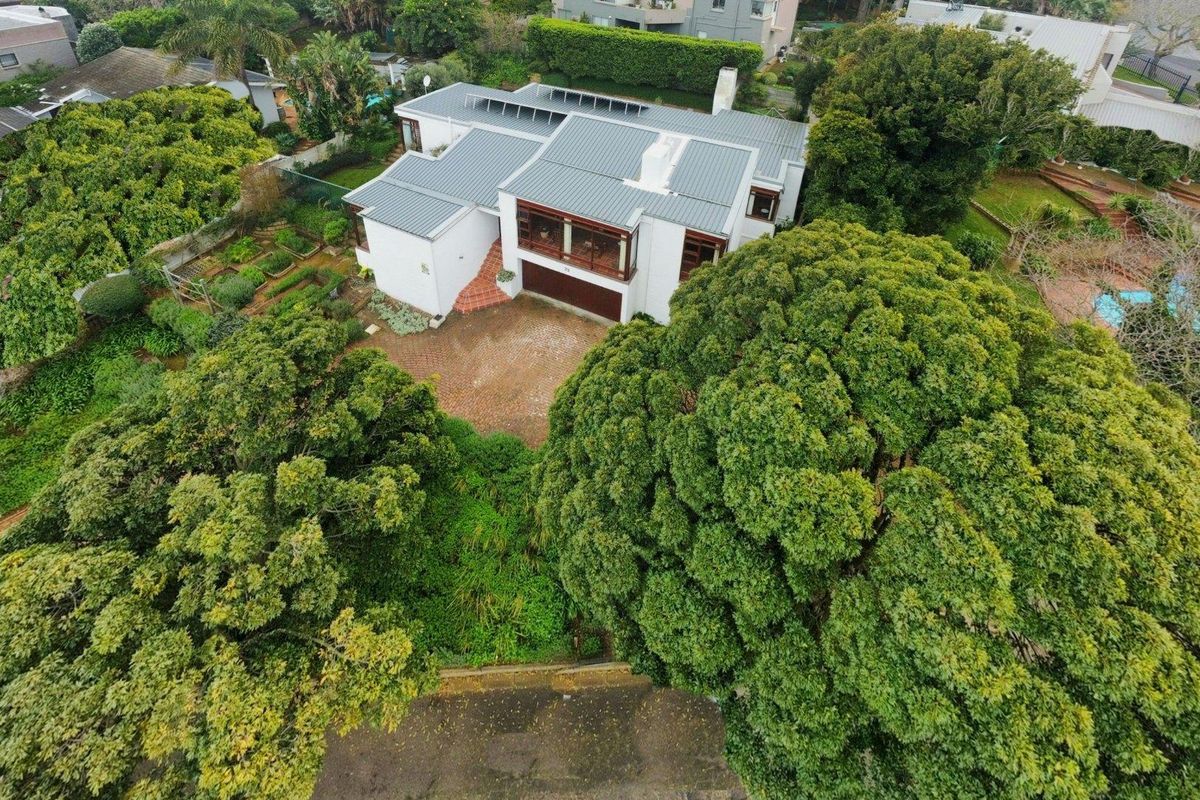 Aerial view of a residential property featuring a metal roof, paved driveway, and extensive surrounding garden with mature trees.
