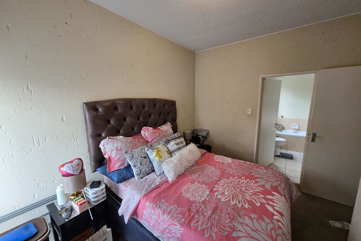 A bedroom featuring textured walls and an en-suite bathroom with a bathtub, offering a functional layout in need of cosmetic updates.