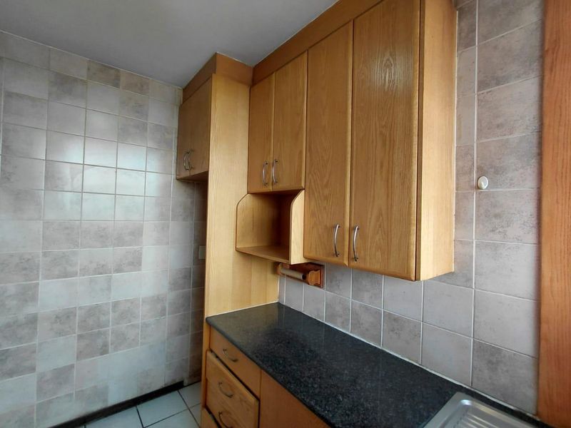 A functional kitchen area featuring wooden cabinetry, dark laminate countertops, and neutral ceramic wall tiling.