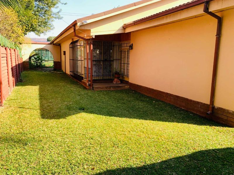 Rear exterior view of the house featuring a lawn, security gates, and established boundary fencing.