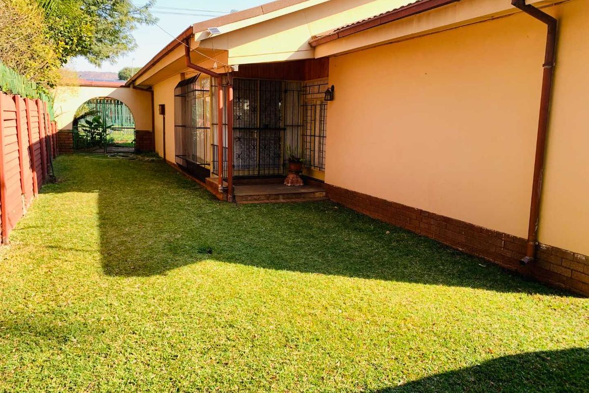 Rear exterior view of the house featuring a lawn, security gates, and established boundary fencing.