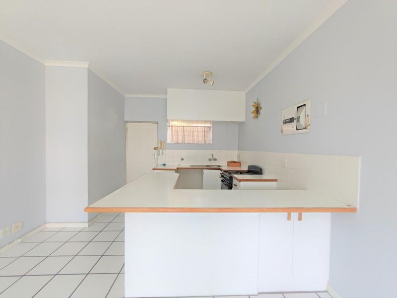 A functional, open-plan kitchen featuring white cabinetry, laminate countertops, a tiled backsplash, and a freestanding stove, presented in a clean, vacant state.