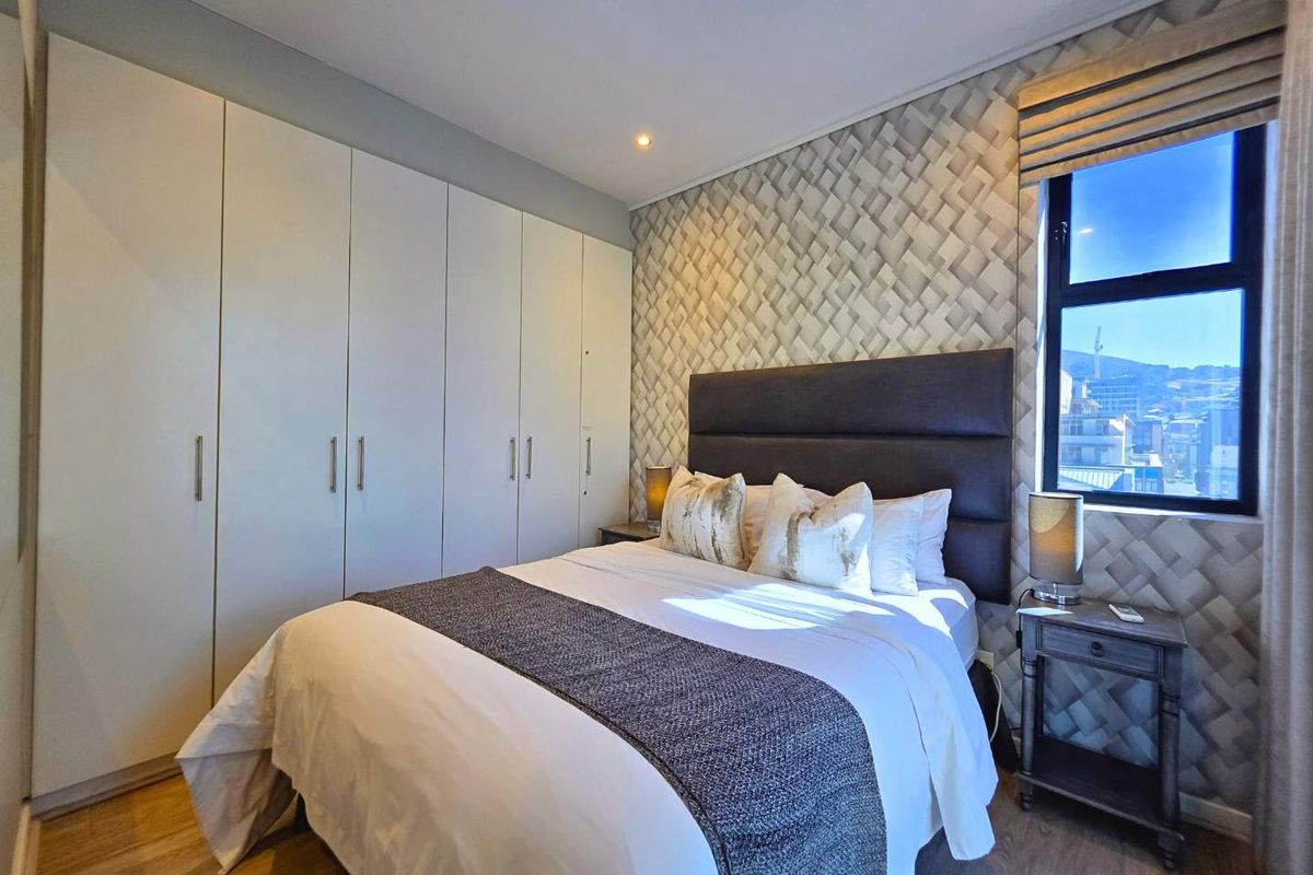 A well-maintained bedroom featuring built-in floor-to-ceiling wardrobes, textured feature wallpaper, and a window with natural light.