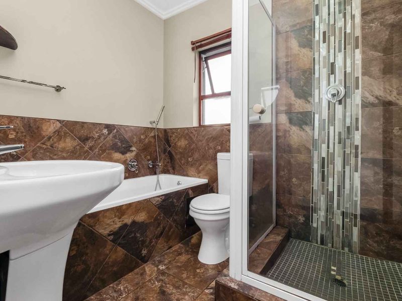 A well-maintained bathroom featuring a pedestal basin, built-in bathtub, and a separate shower enclosure with decorative mosaic tile accents.