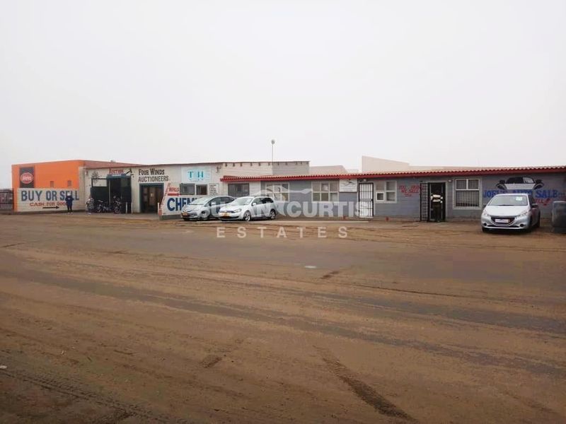Front elevation of an industrial property featuring multiple commercial units with roller doors and security gates, situated on an unpaved access road.