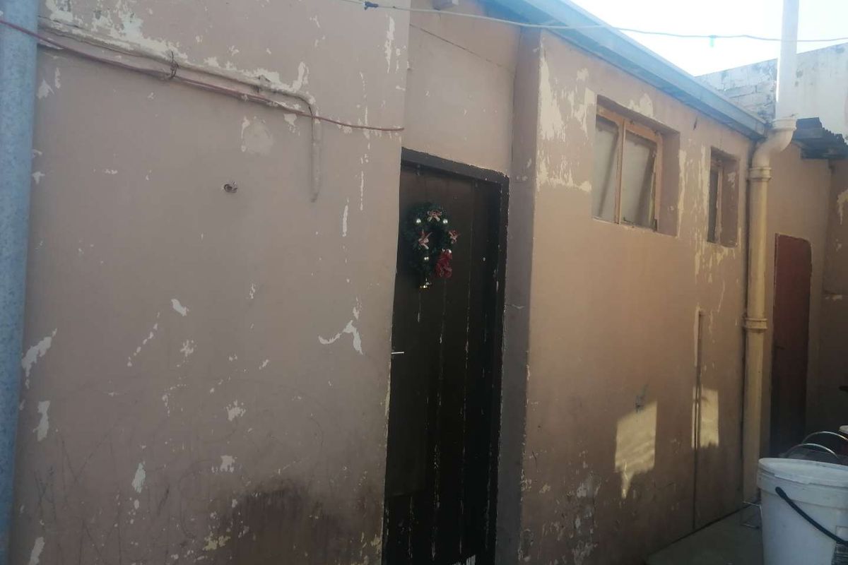 Rear exterior view of the property showing a weathered facade with peeling paint and fixed window frames.