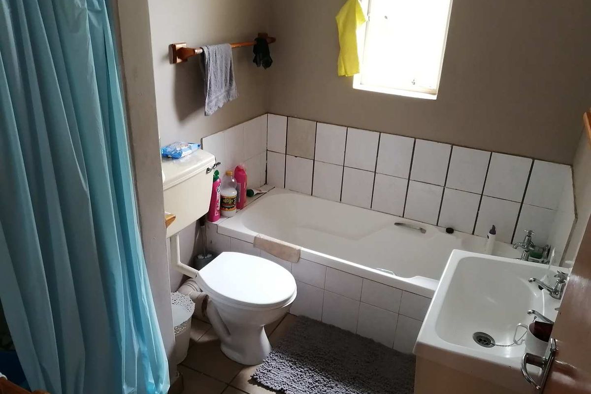 A functional bathroom featuring a bathtub with tiled surround, a standard toilet, and a pedestal sink, requiring some cosmetic updates to the tiling.