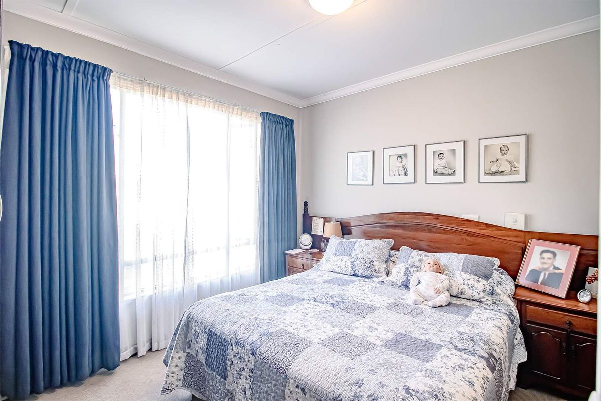 A well-maintained bedroom featuring neutral wall tones, carpeted flooring, and large windows with fitted curtain tracks.