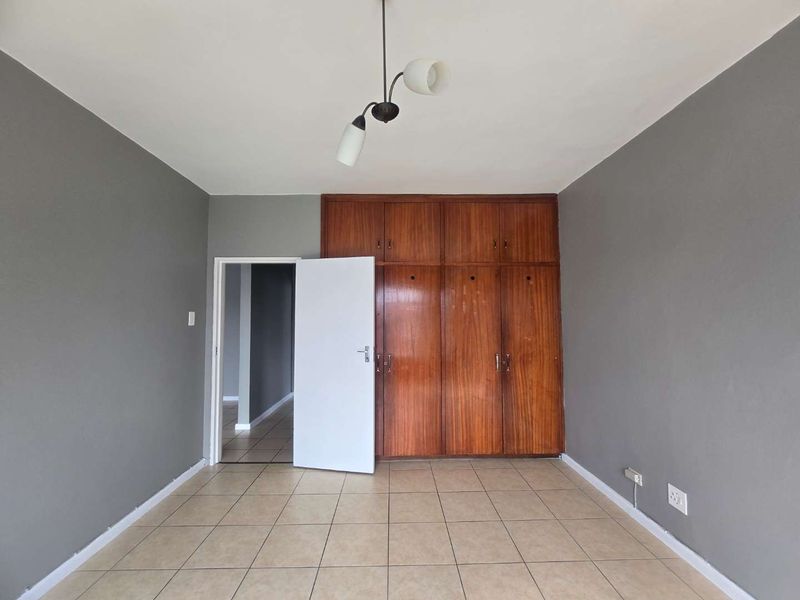 A vacant bedroom featuring tiled flooring, grey painted walls, and floor-to-ceiling built-in wooden cupboards.