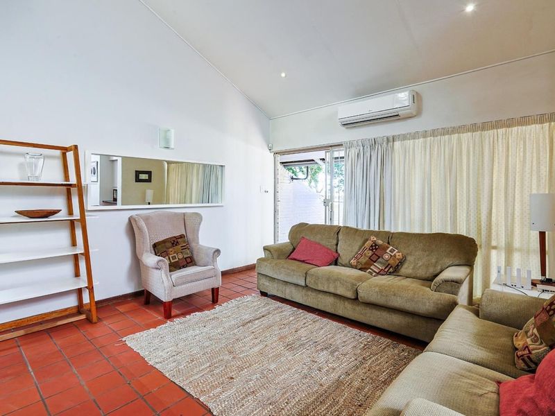 A spacious living room featuring vaulted ceilings, terracotta tile flooring, and a split-system air conditioner, with direct access to an outdoor area.