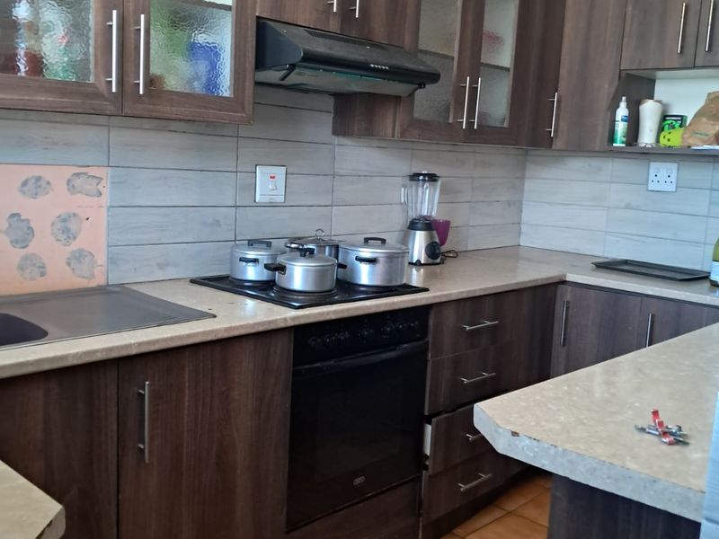 A functional kitchen featuring dark wood-look cabinetry, stone-effect countertops, built-in oven, electric hob, and tiled backsplash with ceramic floor tiles.