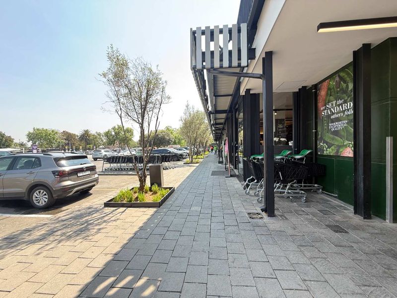 A well-maintained paved walkway leading along the front facade of a retail store, featuring modern structural columns and landscaped planter boxes.