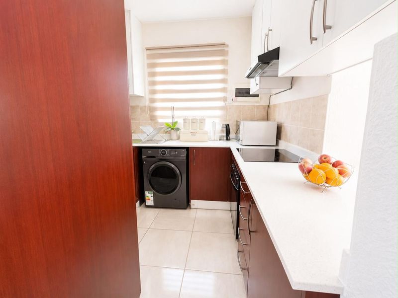A functional scullery featuring dark wood cabinetry, white stone countertops, tiled flooring, and integrated appliances including a hob and extractor fan.