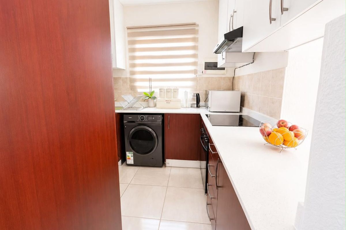 A functional scullery featuring dark wood cabinetry, white stone countertops, tiled flooring, and integrated appliances including a hob and extractor fan.
