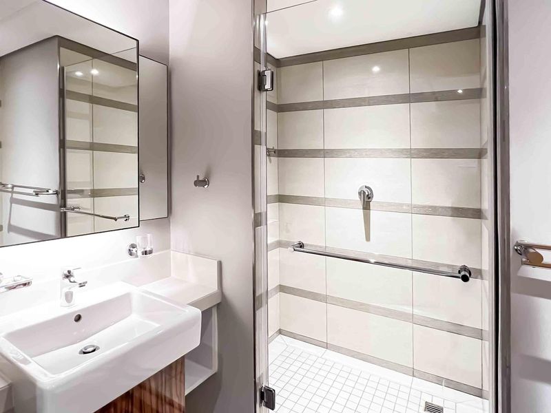Modern bathroom featuring a sleek vanity with basin, large mirror, and a spacious glass-enclosed shower with contemporary tiled finishes.