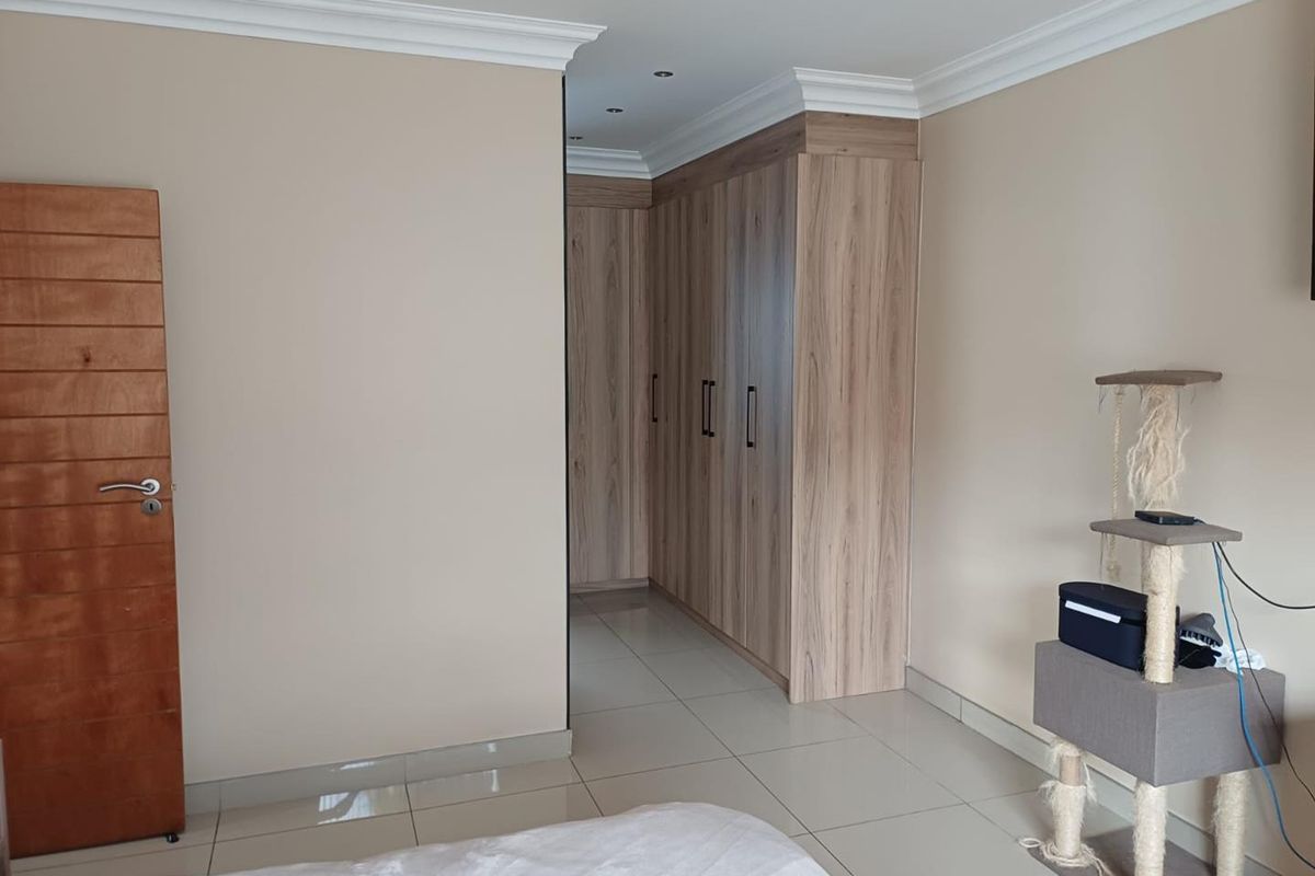 A well-maintained bedroom featuring modern built-in wooden wardrobes, tiled flooring, and decorative ceiling cornices.