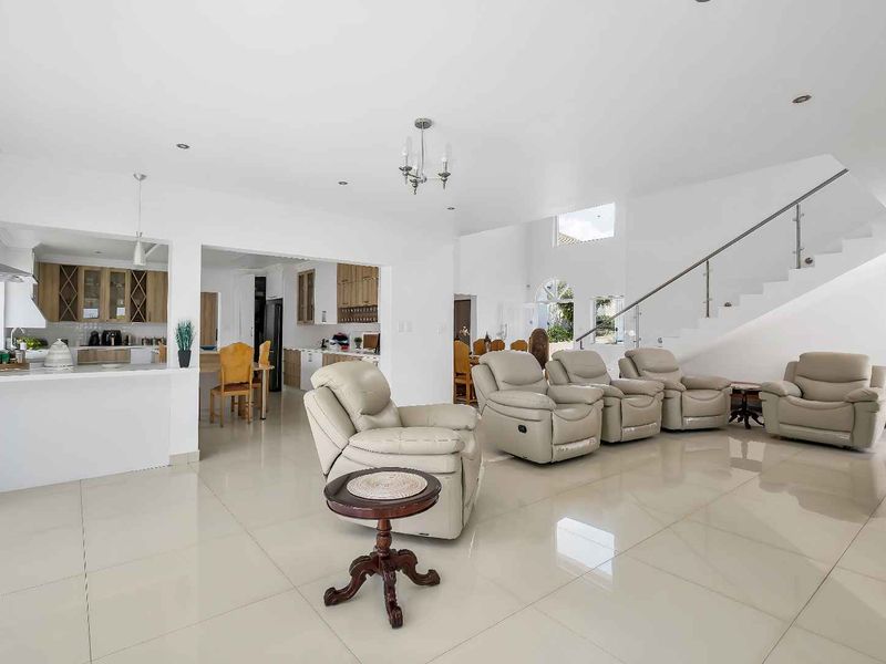 Spacious open-plan living area featuring polished tile flooring, a modern staircase with glass balustrade, and a well-appointed kitchen with ample cabinetry.