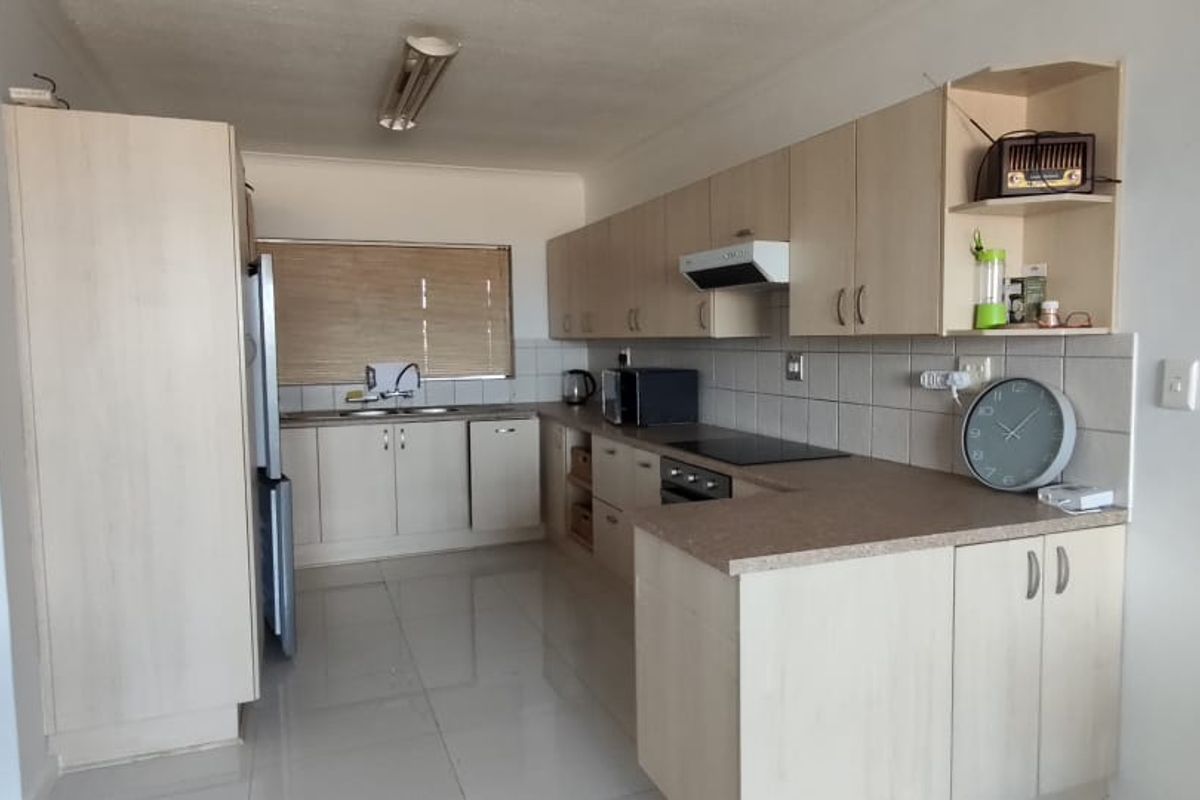 Functional kitchen featuring light-toned built-in cabinetry, laminate countertops, integrated oven and hob, and tiled flooring, offering a practical layout for daily use.