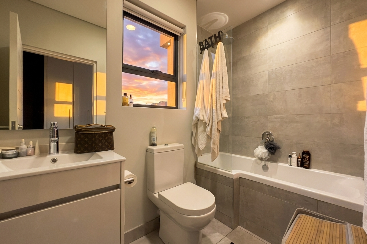 Modern bathroom featuring a vanity with basin, a toilet, and a bathtub with a glass shower screen and tiled surround.