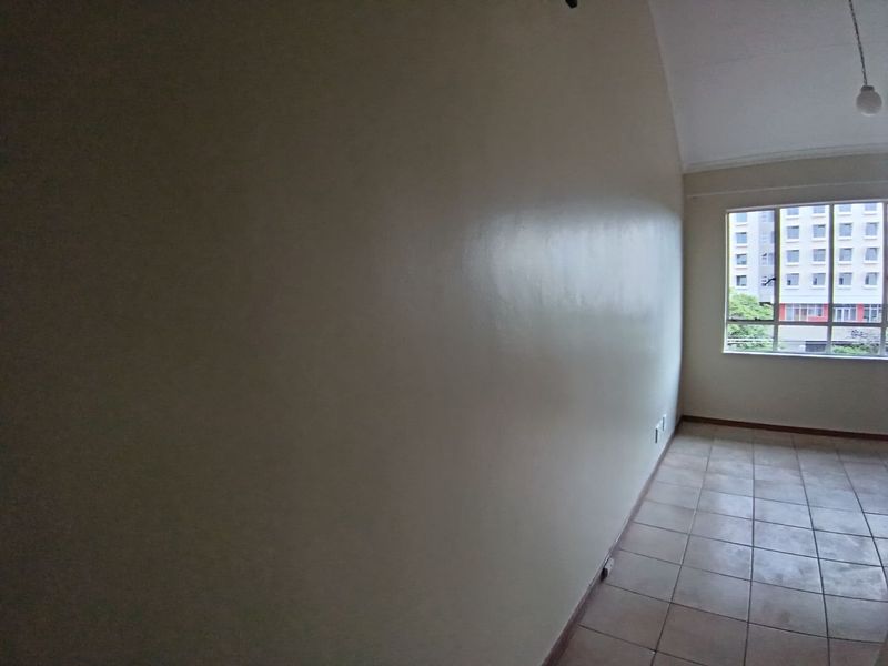 An empty, neutrally painted living area featuring tiled flooring and a large window providing natural light and an urban view.