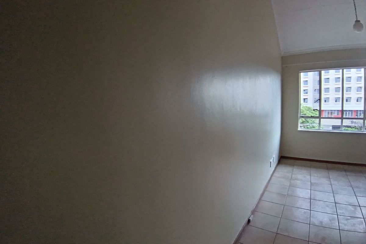 An empty, neutrally painted living area featuring tiled flooring and a large window providing natural light and an urban view.