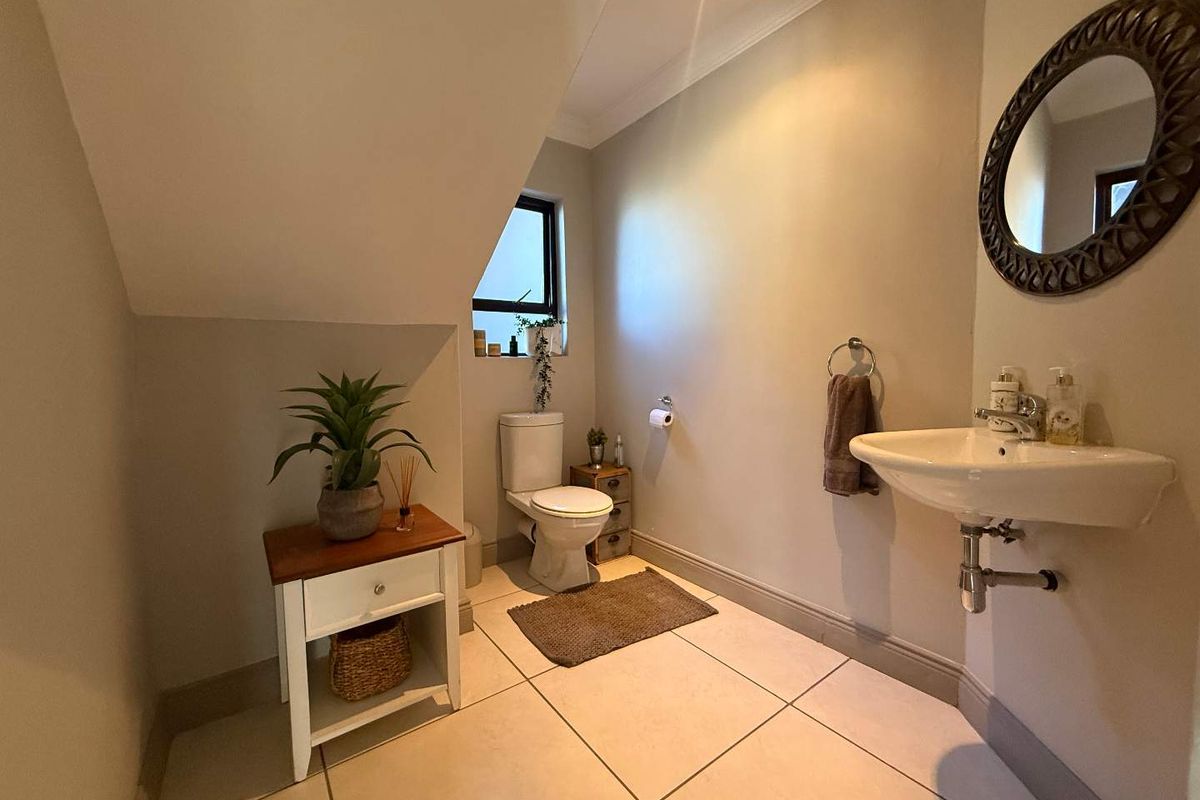 A compact guest bathroom featuring a wall-mounted basin, a standard toilet, and tiled flooring under a sloped ceiling.