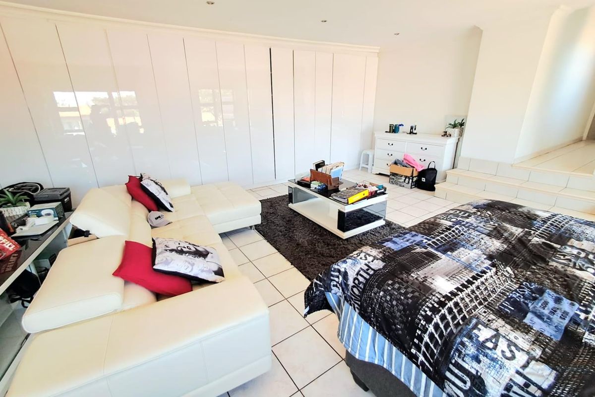 Spacious bedroom featuring extensive white built-in cupboards, tiled flooring, and a raised platform area with recessed downlighting.