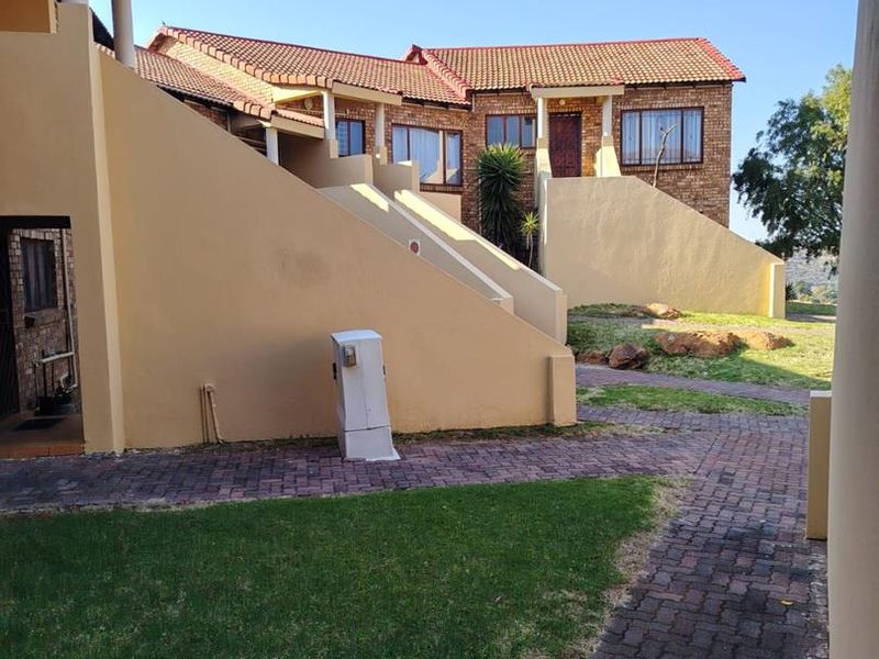 Exterior view of the townhouse complex featuring brick paved pathways, landscaped lawn areas, and external staircases leading to upper levels.