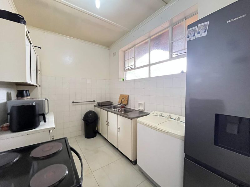 A functional kitchen featuring dated cabinetry, tiled splashbacks, and tiled flooring, offering a practical layout with natural light from a large window.