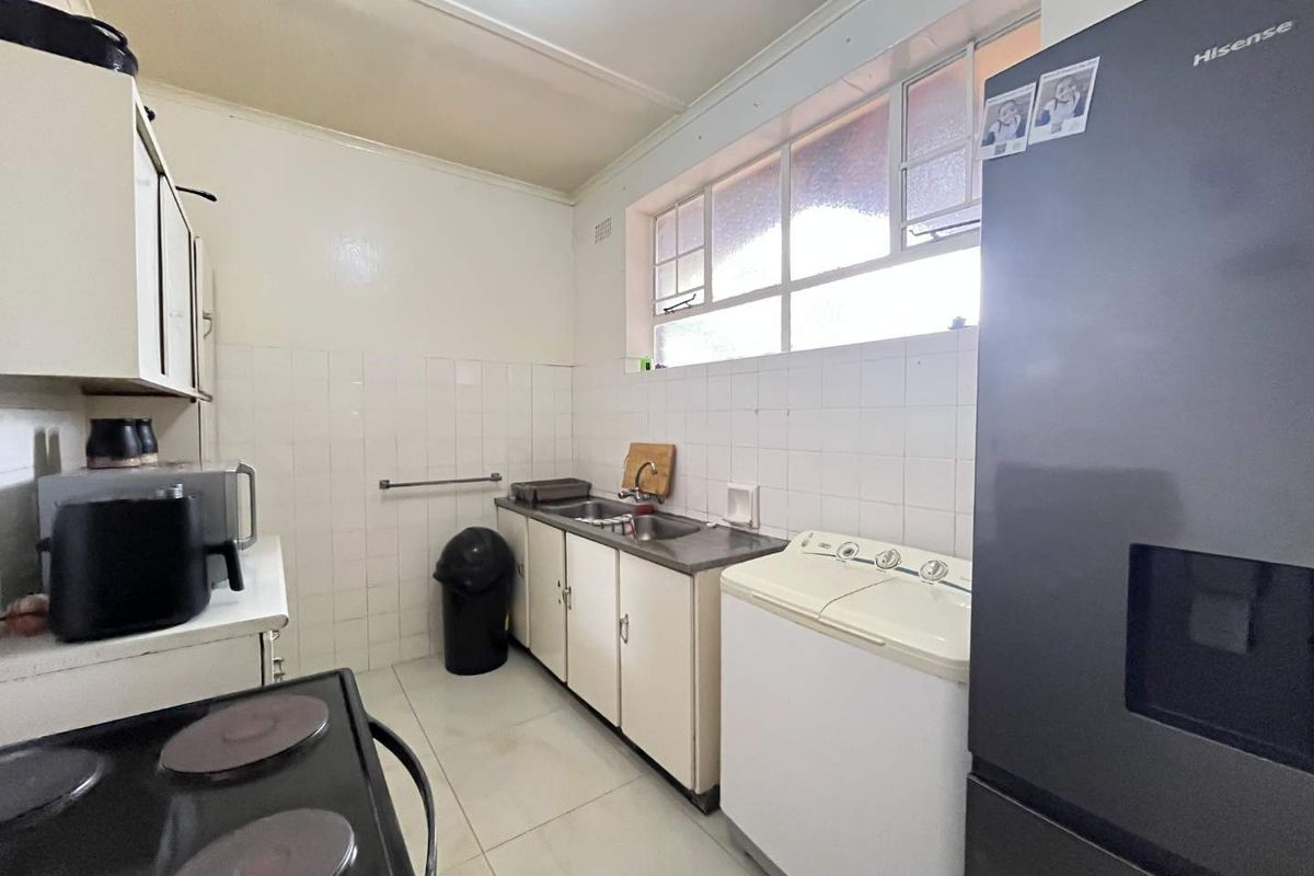 A functional kitchen featuring dated cabinetry, tiled splashbacks, and tiled flooring, offering a practical layout with natural light from a large window.