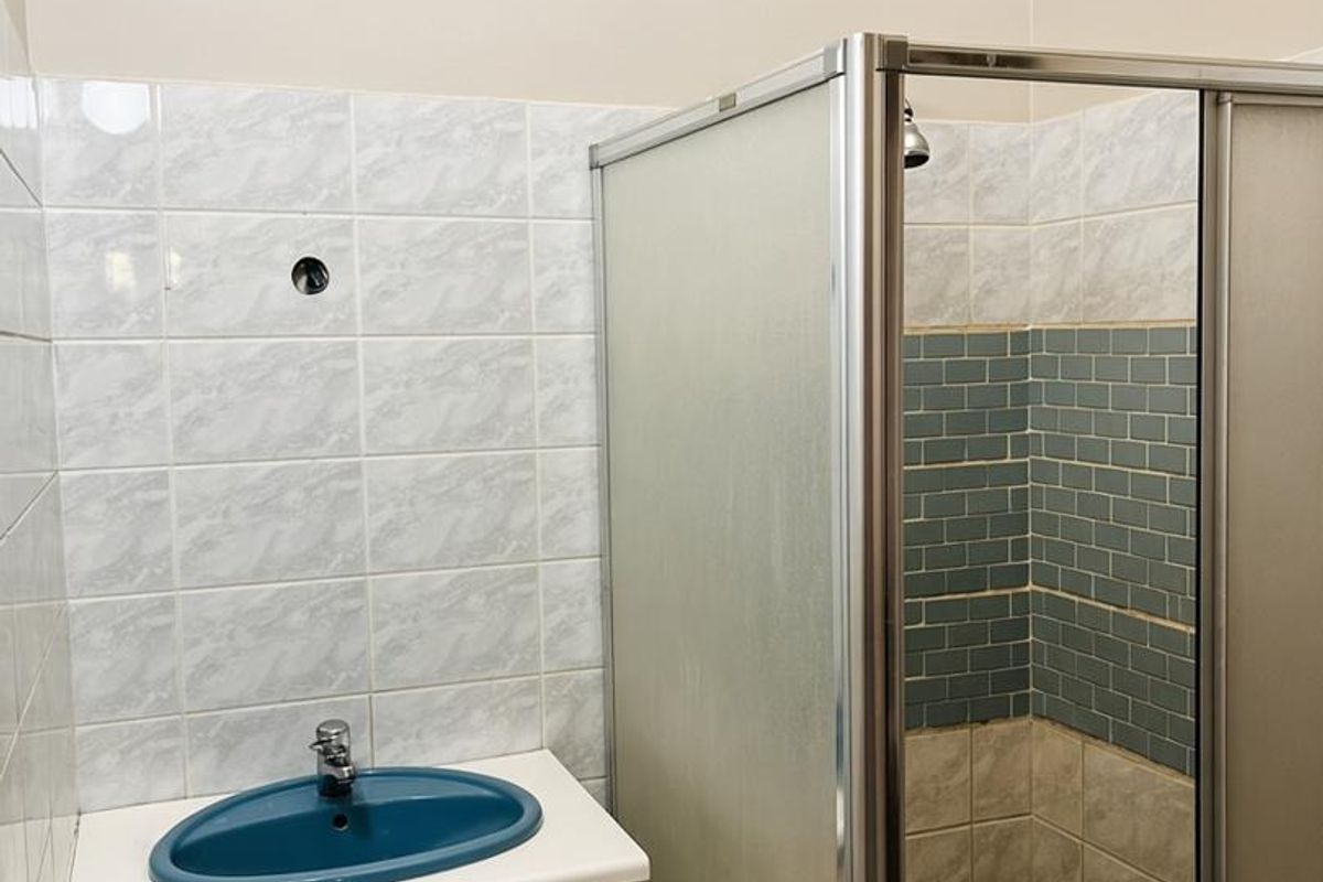 A functional bathroom featuring a vanity unit with a blue sink and a separate shower enclosure with tiled walls.
