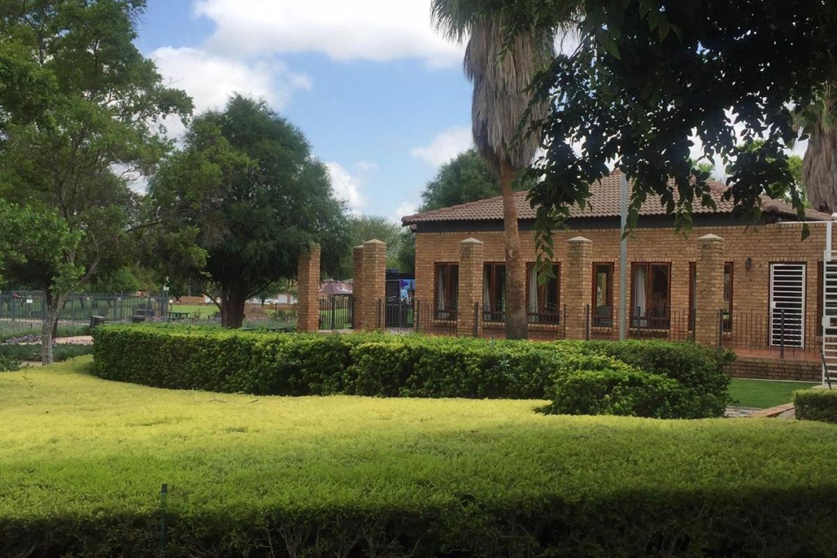 A view of the townhouse exterior featuring face-brick facade, tiled roof, and well-maintained landscaped garden with manicured hedges.