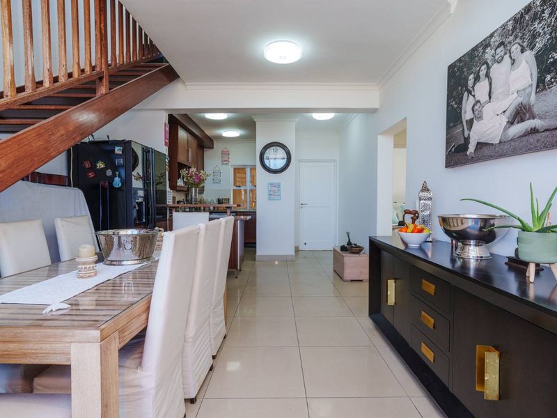 Open-plan living and dining area featuring tiled flooring, a wooden staircase, and a view through to the kitchen space.