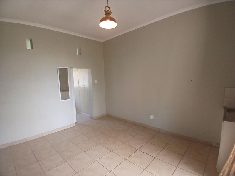 A bright, empty living area featuring neutral tiled flooring, cove cornicing, and access to a built-in cupboard space.