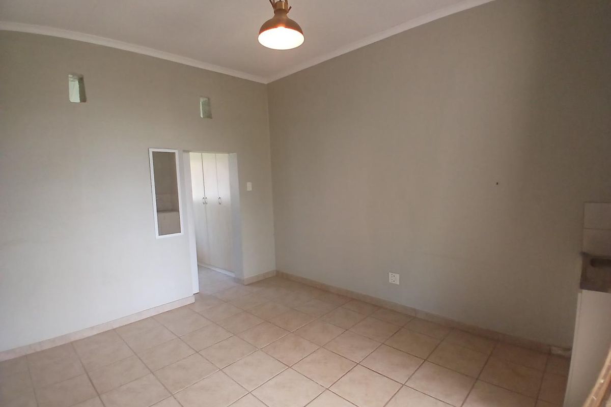 A bright, empty living area featuring neutral tiled flooring, cove cornicing, and access to a built-in cupboard space.