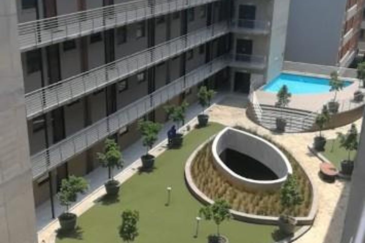 Aerial view of an apartment complex courtyard featuring a swimming pool, landscaped garden areas, and multi-level balcony walkways.