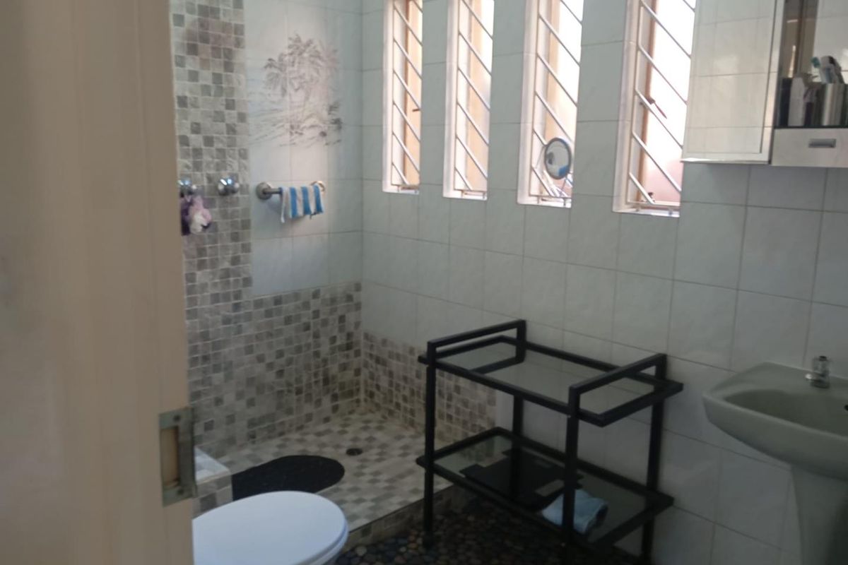 A functional bathroom featuring a walk-in shower with mosaic tile accents, a pedestal sink, and multiple windows providing natural light.