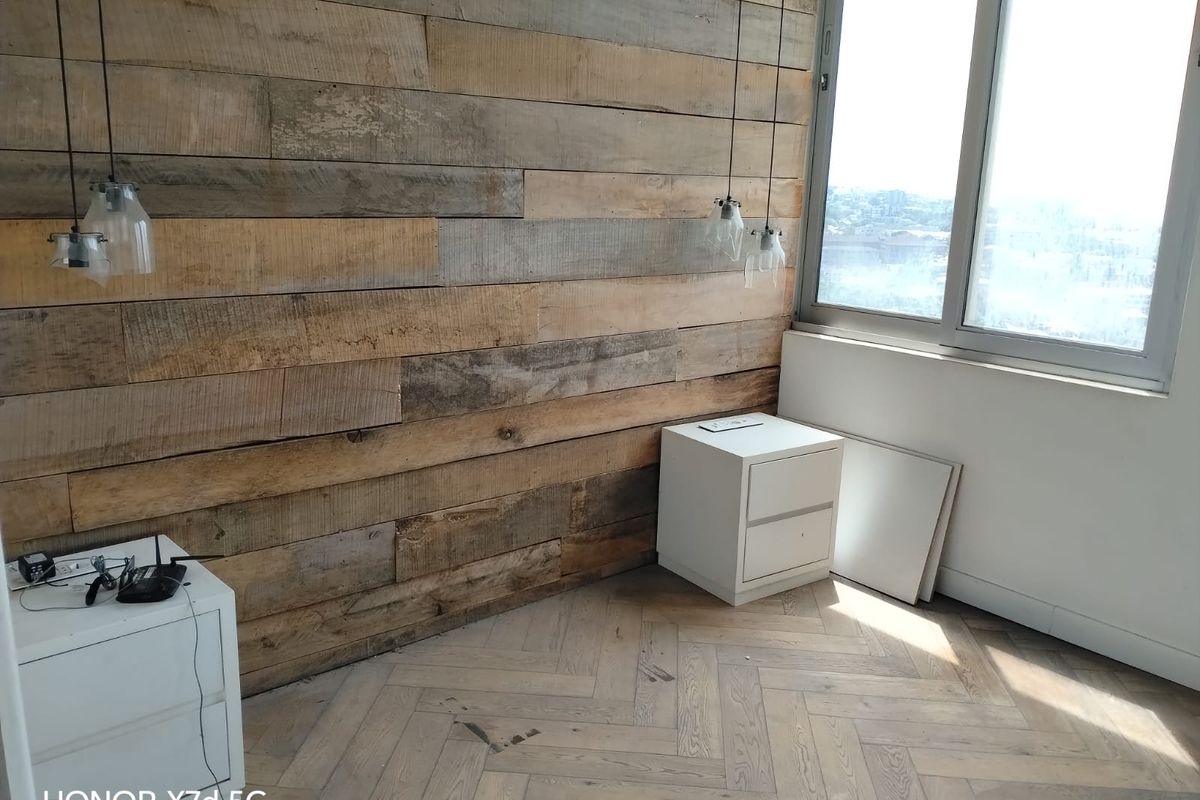 Bedroom featuring a distinctive reclaimed timber feature wall, herringbone wood flooring, and large windows providing natural light and elevated views.