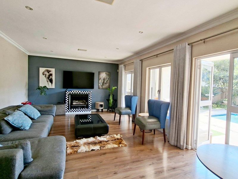Spacious living room featuring laminate flooring, a feature fireplace, and large sliding glass doors providing direct access to the outdoor pool area.