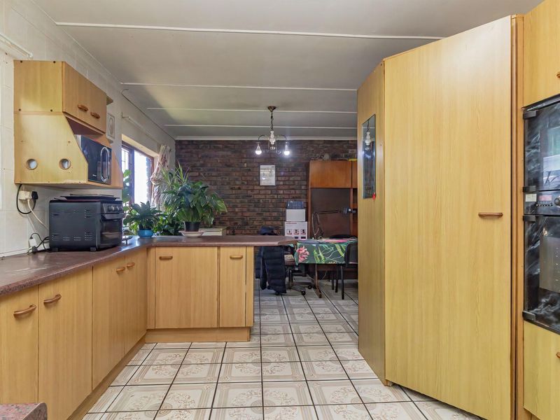 A functional kitchen featuring light wood-look cabinetry, laminate countertops, a built-in double oven, and a distinctive exposed brick wall in the adjacent dining area.