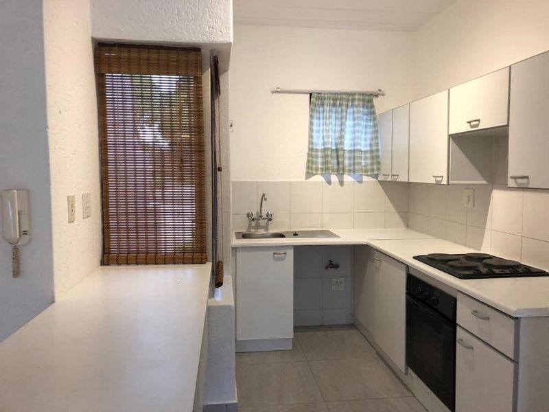 A functional kitchen featuring built-in cabinetry, a stainless steel sink, an integrated oven, and an electric hob with a tiled backsplash.