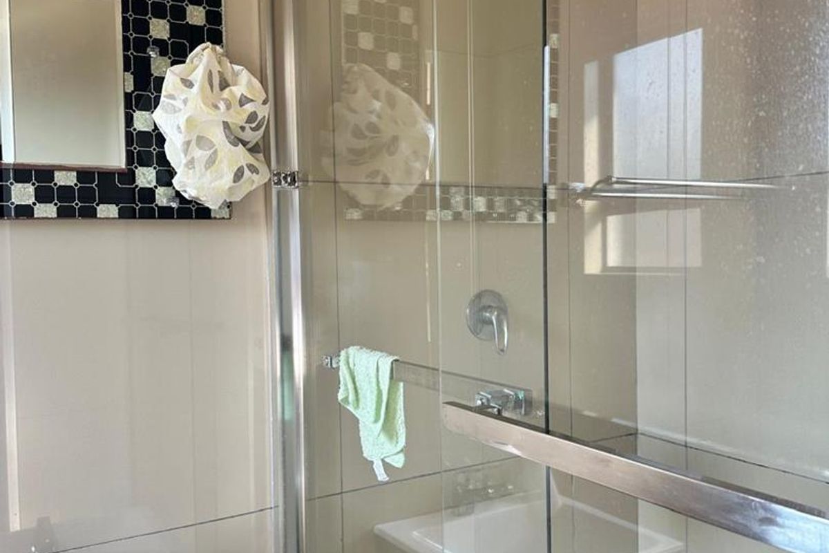 A modern bathroom featuring a glass-enclosed shower with a rain shower head, a wall-mounted vanity basin, and decorative mosaic tile accents.