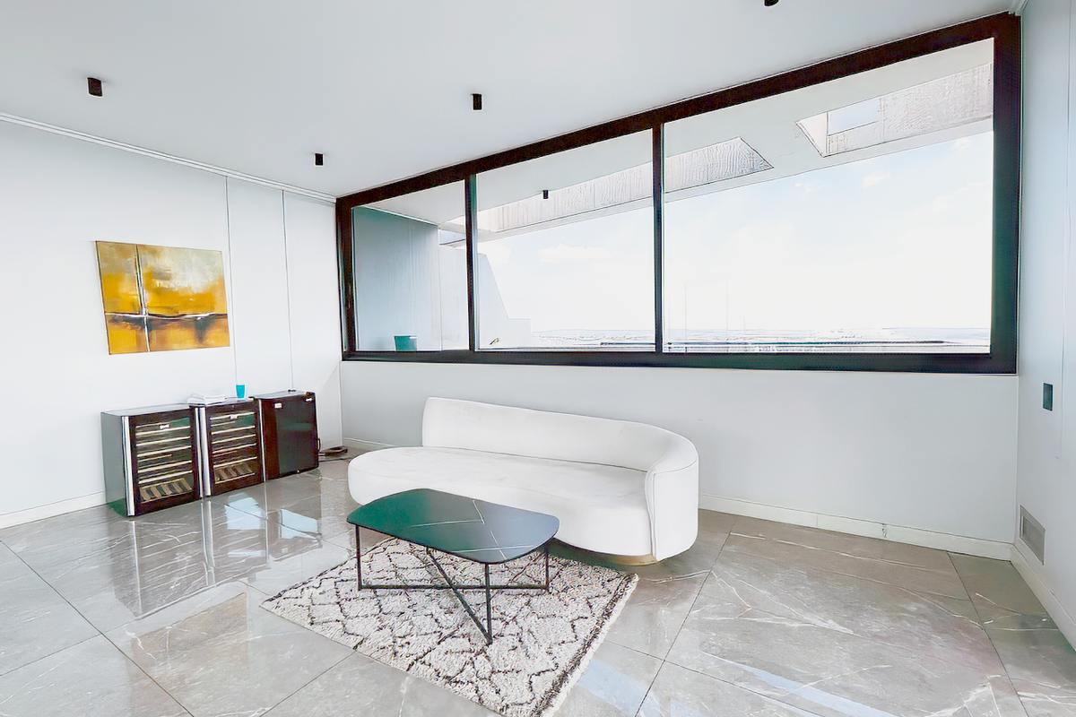 Modern living area featuring large floor-to-ceiling windows with expansive views, polished marble-look tile flooring, and recessed ceiling spotlights.
