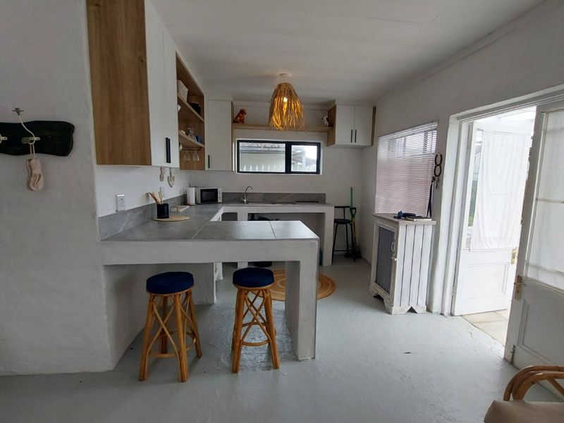A compact kitchen featuring built-in cabinetry, concrete-style countertops, a breakfast bar, and direct access to an outdoor area through a glass panel door.
