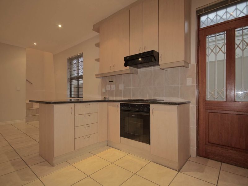 A functional kitchen featuring light wood cabinetry, granite countertops, built-in oven and hob, tiled flooring, and direct access to the exterior via a timber door.