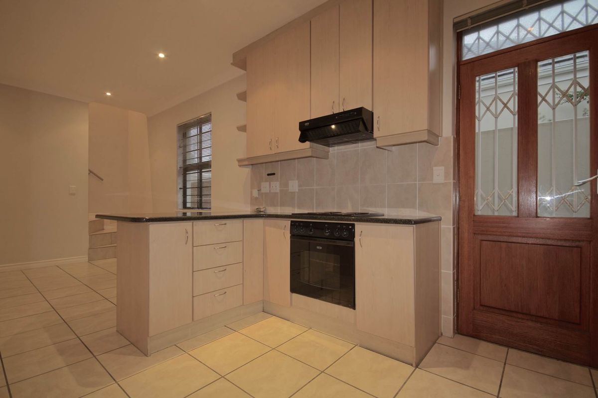 A functional kitchen featuring light wood cabinetry, granite countertops, built-in oven and hob, tiled flooring, and direct access to the exterior via a timber door.