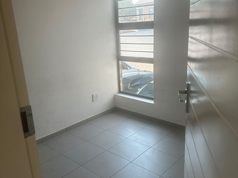 A compact, empty bedroom featuring neutral tiled flooring, a horizontal sliding window with security bars, and clean white walls.
